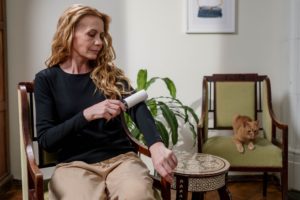 Woman removing cat hair from her clothing as she deals with cat shedding.